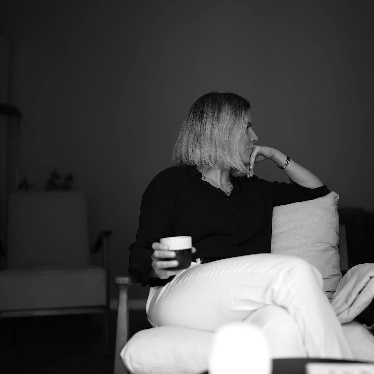 Anna Wyganowska-Błażejewska z kubkiem w dłoni siedzi w fotelu i patrzy w okno, zdjęcie czarno-białe
