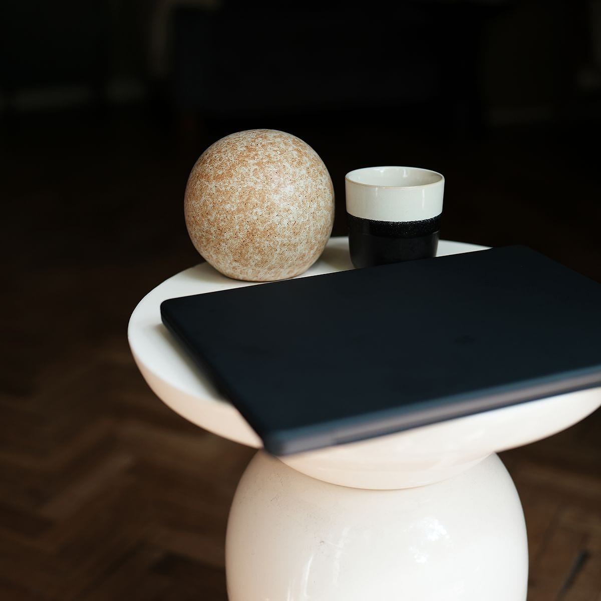 Zamknięty laptop na kremowym stoliku obok kubka i kamiennej kuli